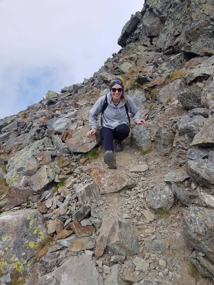 Anna Pro strahlt in die Kamera. Sie ist gerade auf einem Berg biem Wandern unterwegs.